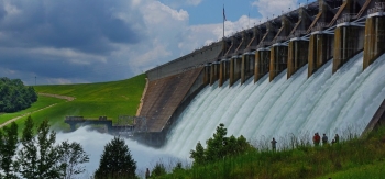 hydropower dam with several people n the foreground and a lush green landscape in the background