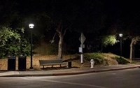Photo of a sidewalk at night with a bench in the middle and streetlights on either side.
