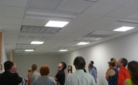 Photo of a group of people in a room looking up at troffer lights in the ceiling.