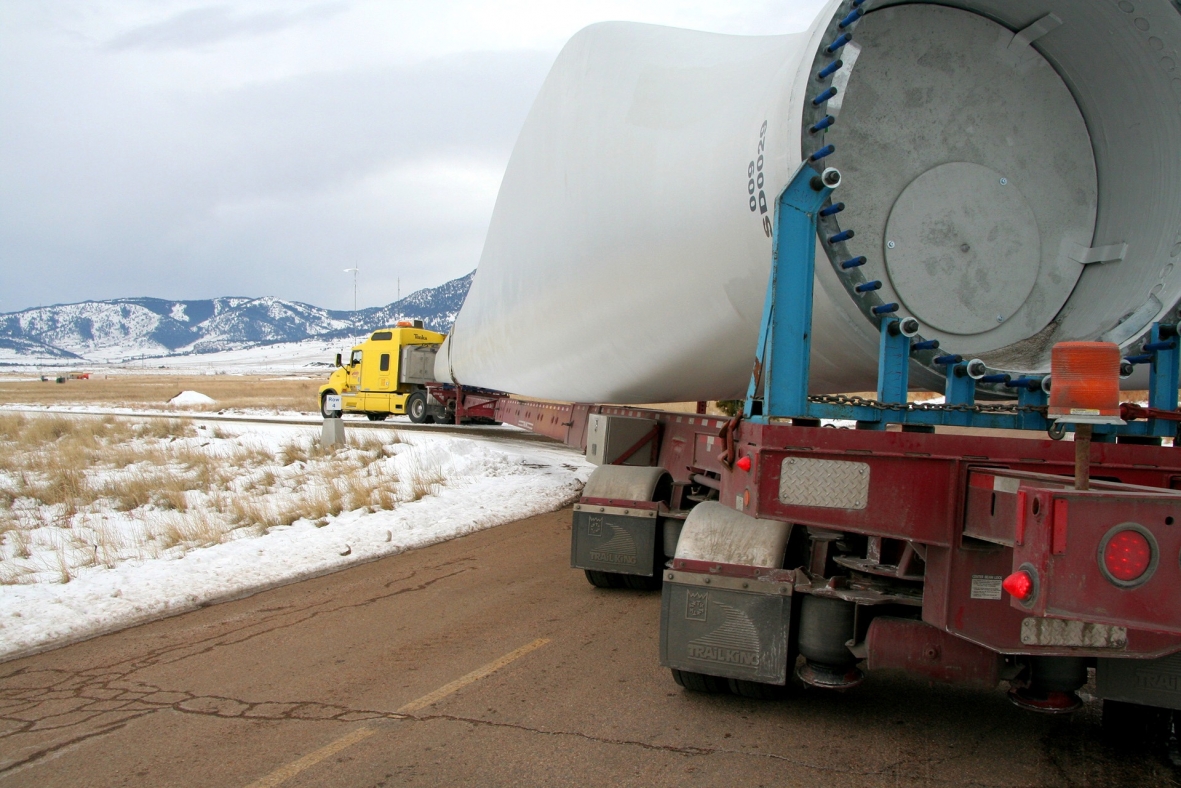 Photo of a large wind turbine blade being carried on the bed of a truck.