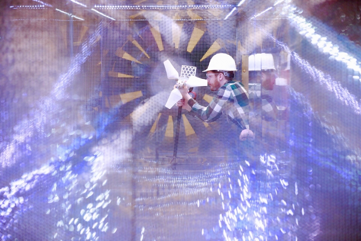 A man in a hard hat using a screwdriver to adjust a small wind turbine.