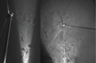 Traces of rich coherent flow structures behind a 2.5-MW wind turbine at the EOLOS Wind Energy Research Field Station in Rosemount, Minnesota, are visualized by the snowflakes illuminated in a light sheet parallel (left) and perpendicular (right) to the wind direction. These flow structures include tip vortices and trailing sheet vortices generated from the rotating turbine blades, and the vortices shed from the turbine hub and tower. <em>Photo by Jiarong Hong and Michele Guala</em> A blurry, black and white photo of wind turbines in a blizzard.
