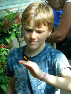 Issac Kisker. Photo Courtesy of the Kisker family. Photo of a young boy outdoors looking at a butterfly on his hand.