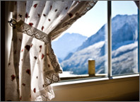 Photo of a window with the curtains open. Sun is shining into the room and snow-covered mountains are visible outside. Copyright iStockphoto.com/Giorgio Fochesato.